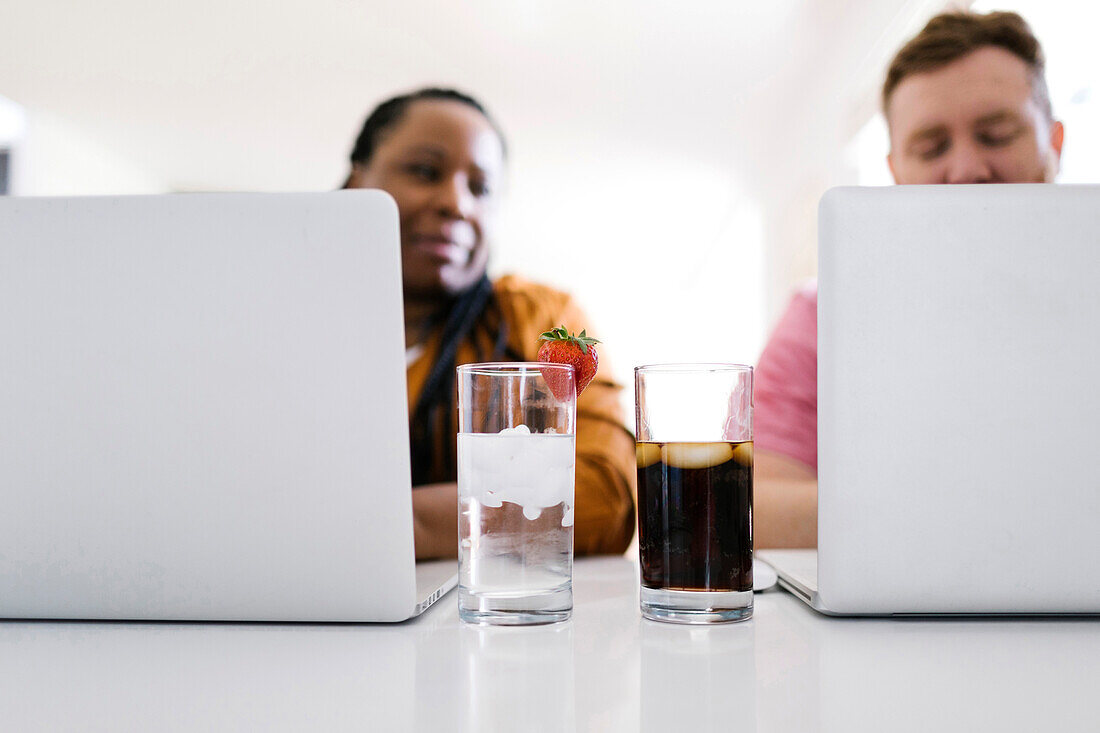 Wasser und Soda in Gläsern zwischen Mann und Frau, die an Laptops arbeiten