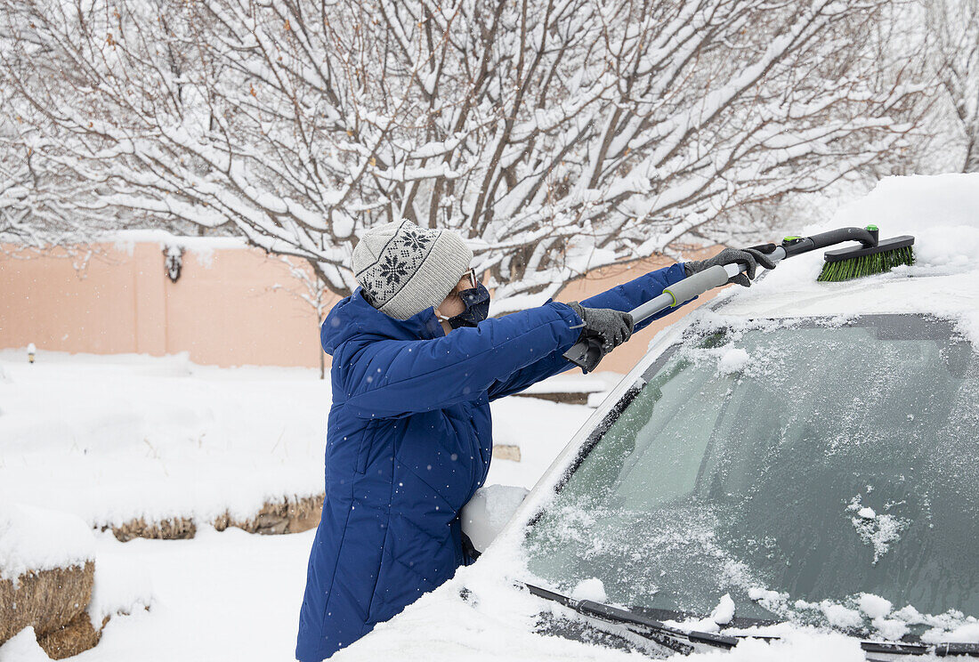 USA, New Mexico, Santa Fe, Frau mit Gesichtsmaske entfernt Schnee aus Auto