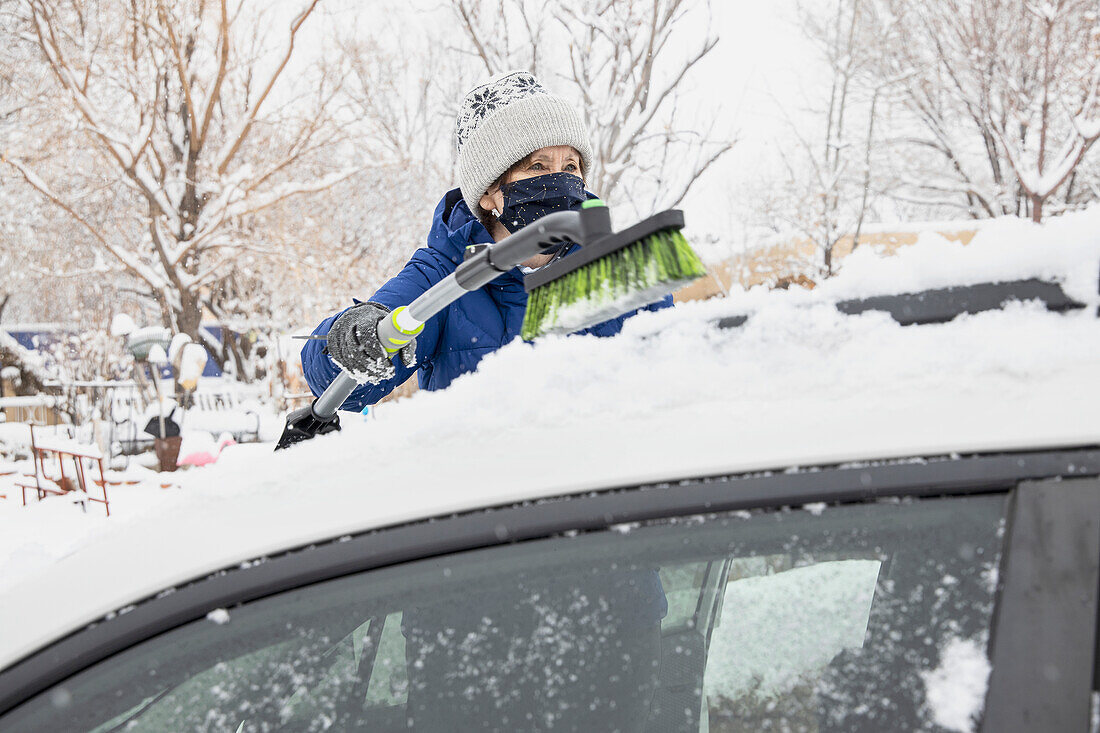 USA, New Mexico, Santa Fe, Woman in face mask removing snow from car
