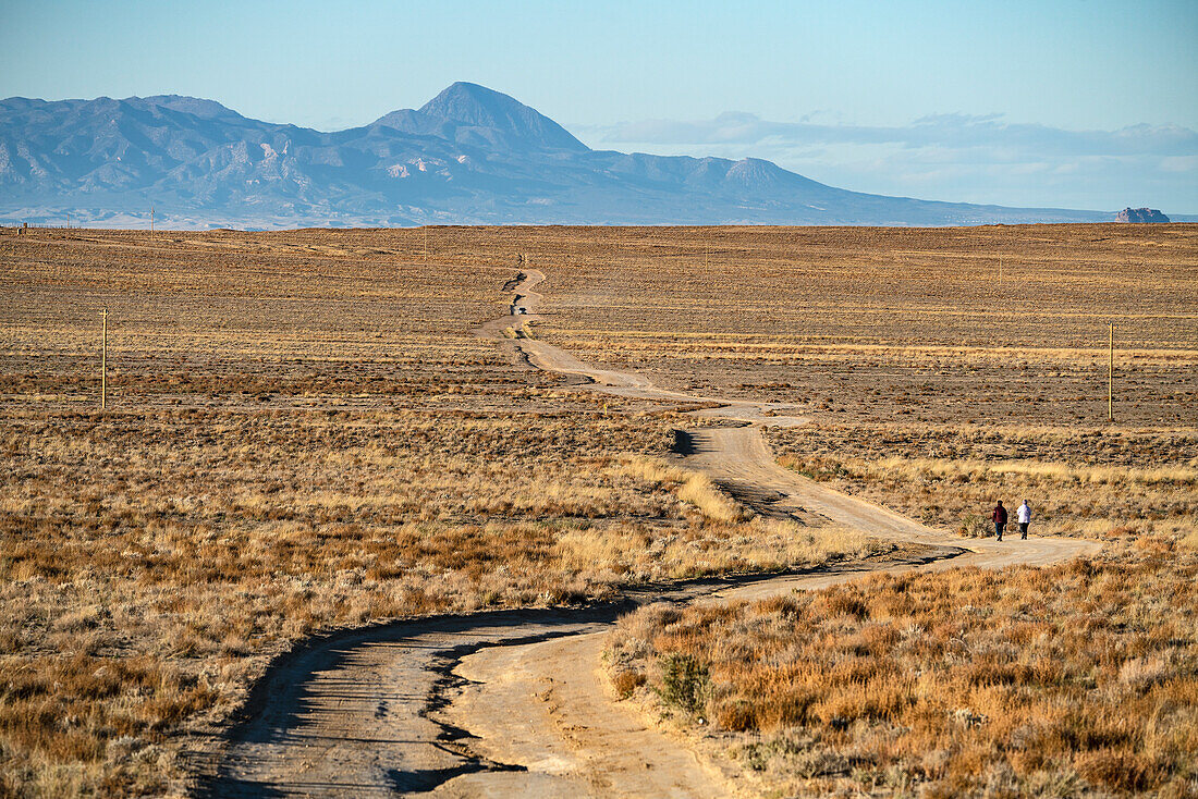 USA, New Mexico, Shiprock, Schotterstraße in Wüstenlandschaft, zwei Frauen in der Ferne