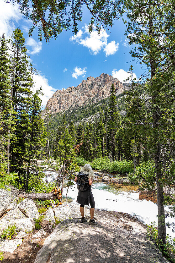 USA, Idaho, Stanley, Ältere Wanderin schaut auf rauschenden Bach in den Sawtooth Mountains