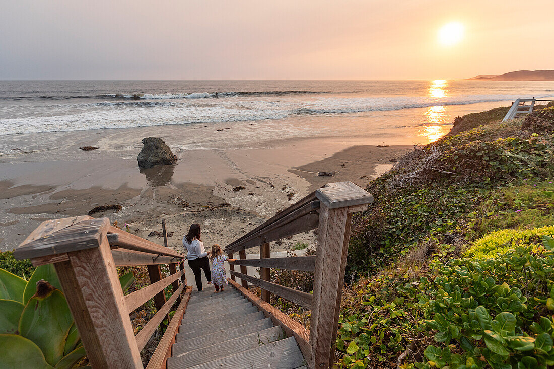 USA, Kalifornien, Cayucos, Mutter und Tochter (4-5) auf der Treppe zum Strand bei Sonnenuntergang