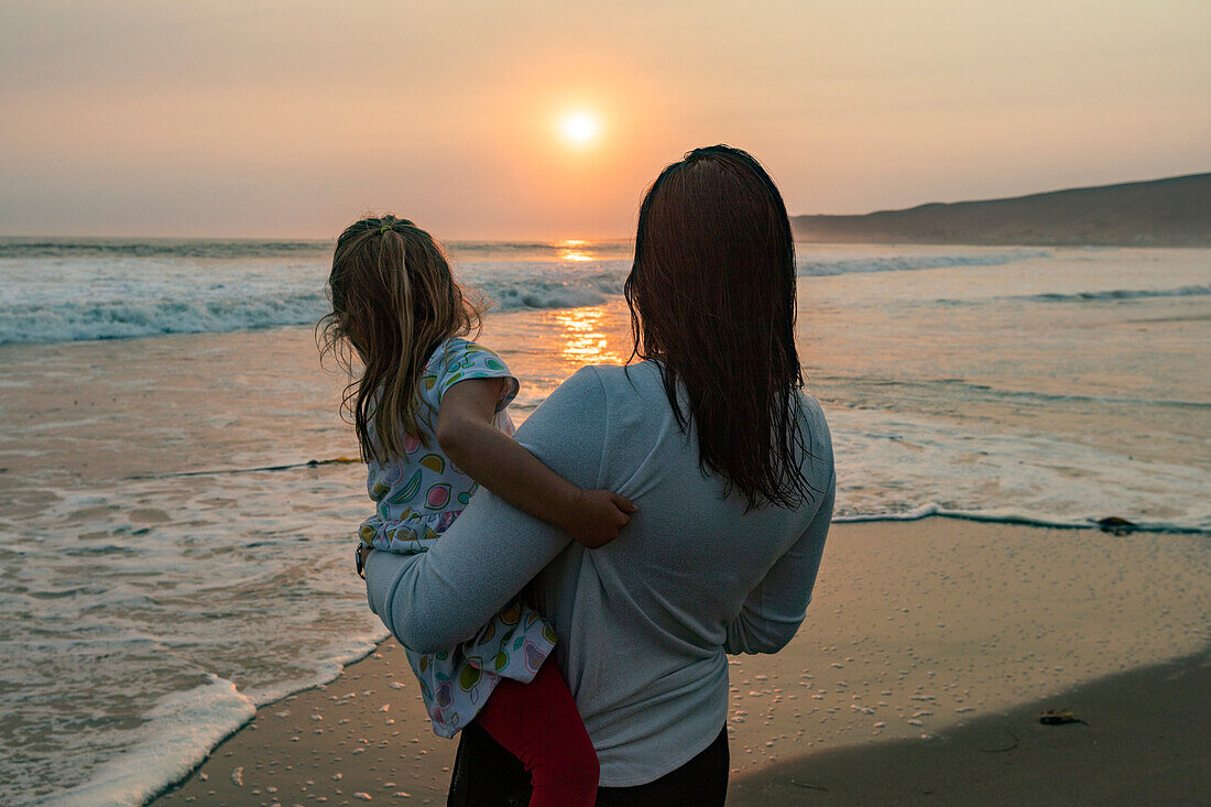 Mother and daughter (4-5) on beach at sunset