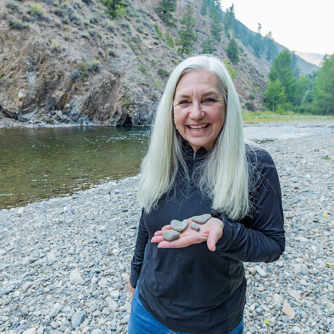 USA, Idaho, Hailey, Portrait of smiling woman holding heart shaped river rocks at Big Wood River