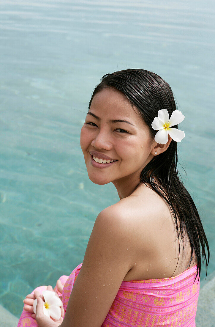 Porträt einer lächelnden Frau mit Frangipani-Blüte im Haar