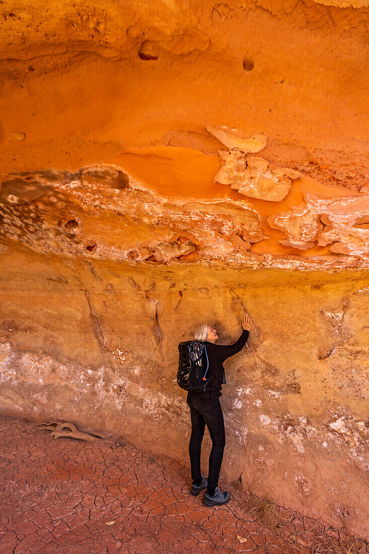 USA, Utah, Escalante, Frau berührt Sandstein-Höhlenwand im Grand Staircase-Escalante National Monument