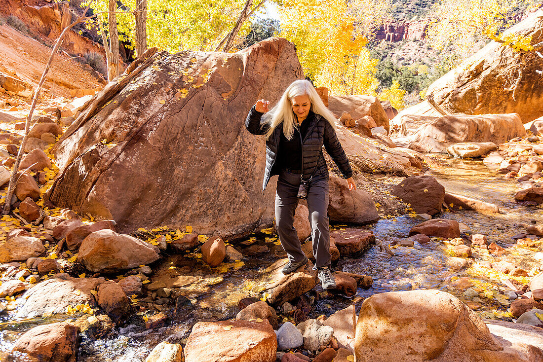 USA, Utah, Zion National Park, Senior female hiker crossing creek