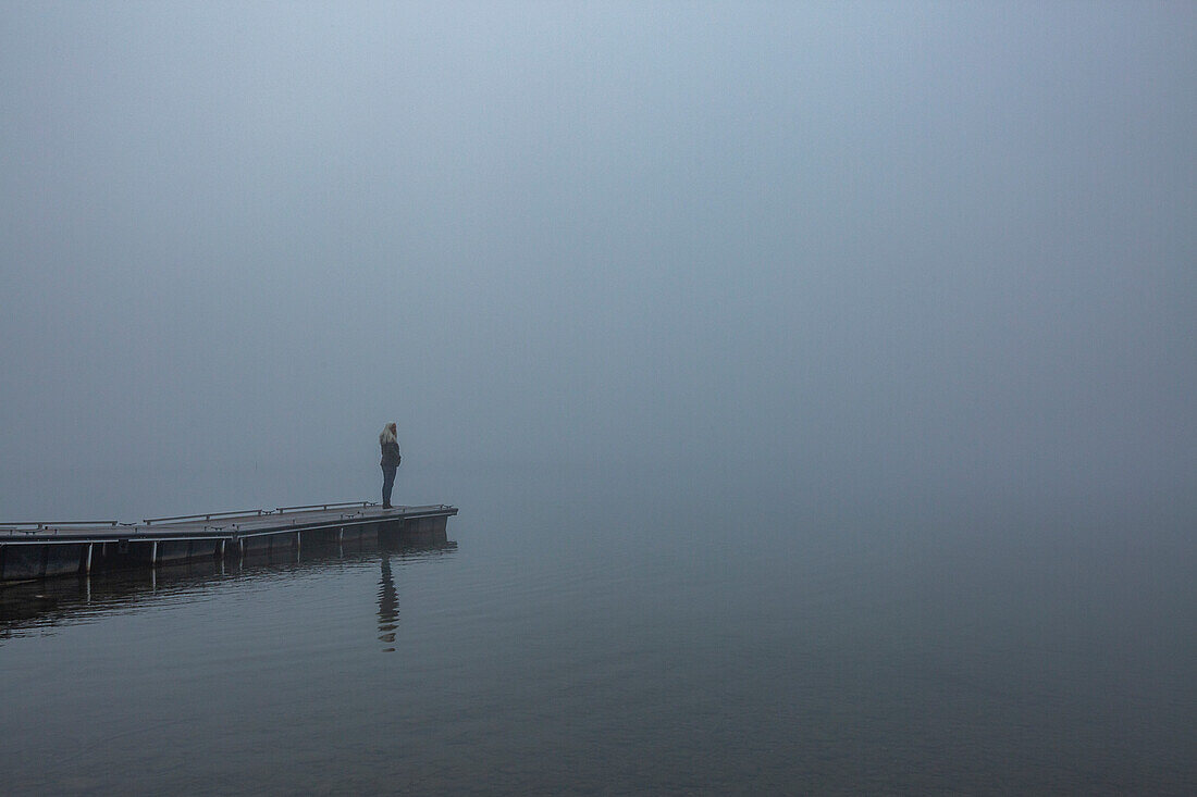 Frau steht morgens auf einem Steg am See