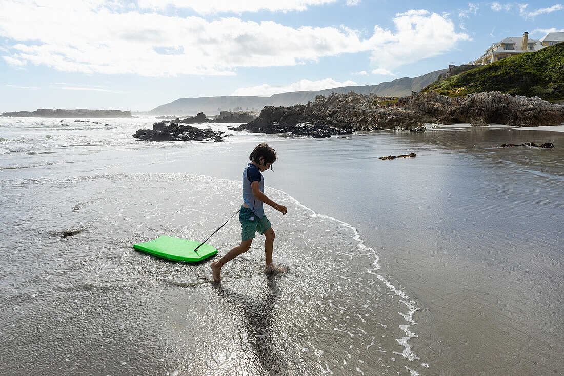 South Africa, Hermanus, Boy (8-9) with surfboard on beach