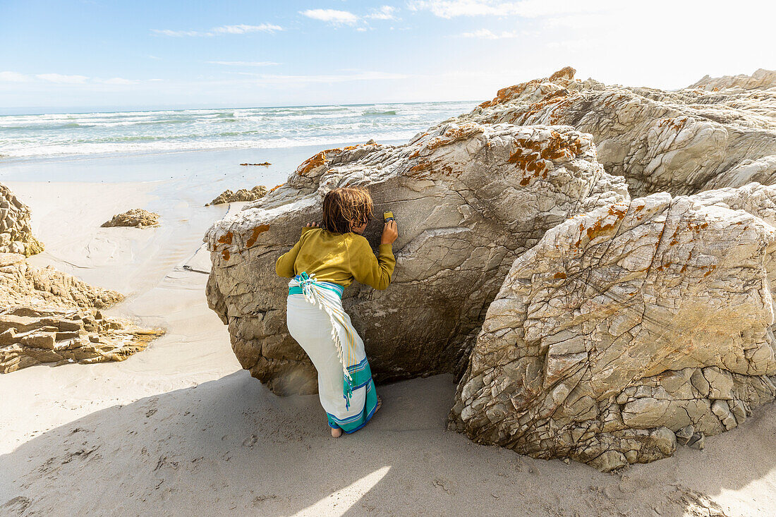 South Africa, Hermanus, Boy (8-9) hiding behind rock on beach