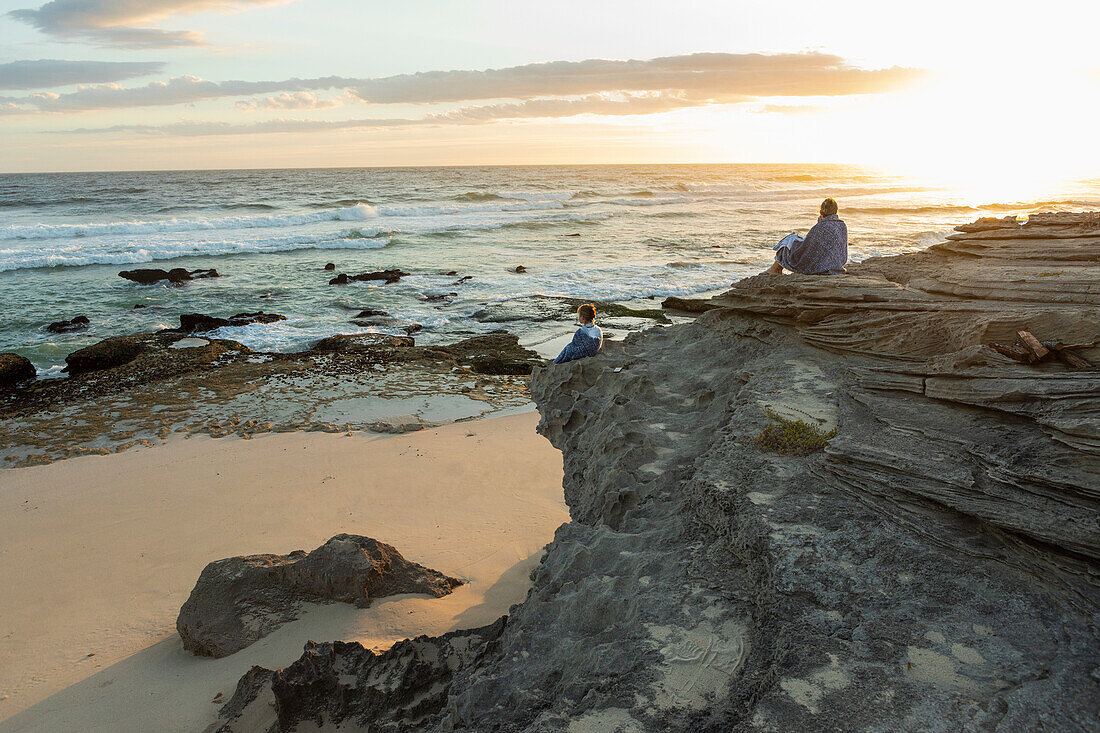 Südafrika, Westkap, Mutter und Tochter (16-17) sitzen bei Sonnenuntergang am Strand im Lekkerwater Nature Reserve