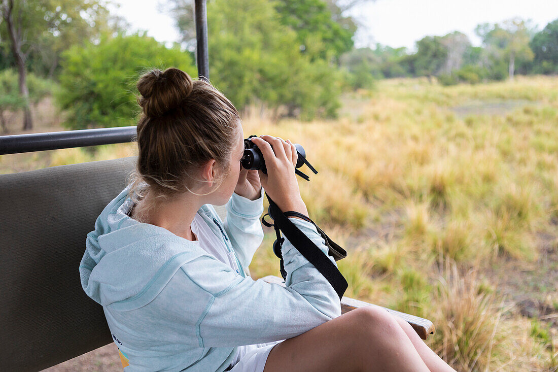 Africa, Zambia, Girl (16-17) in safari vehicle using binoculars