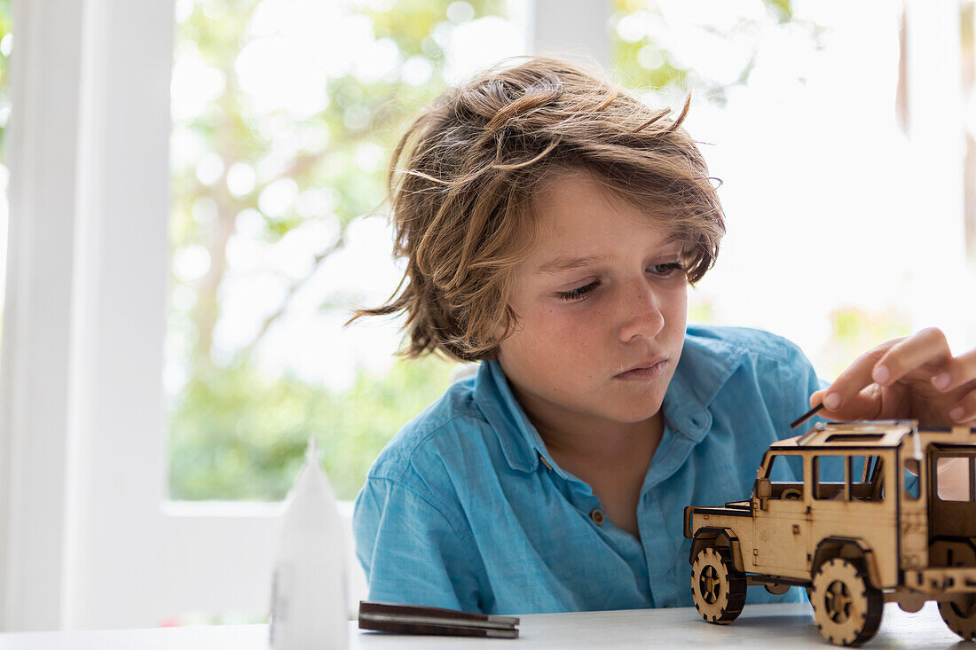 Junge (8-9) baut zu Hause ein Spielzeugauto aus Holz