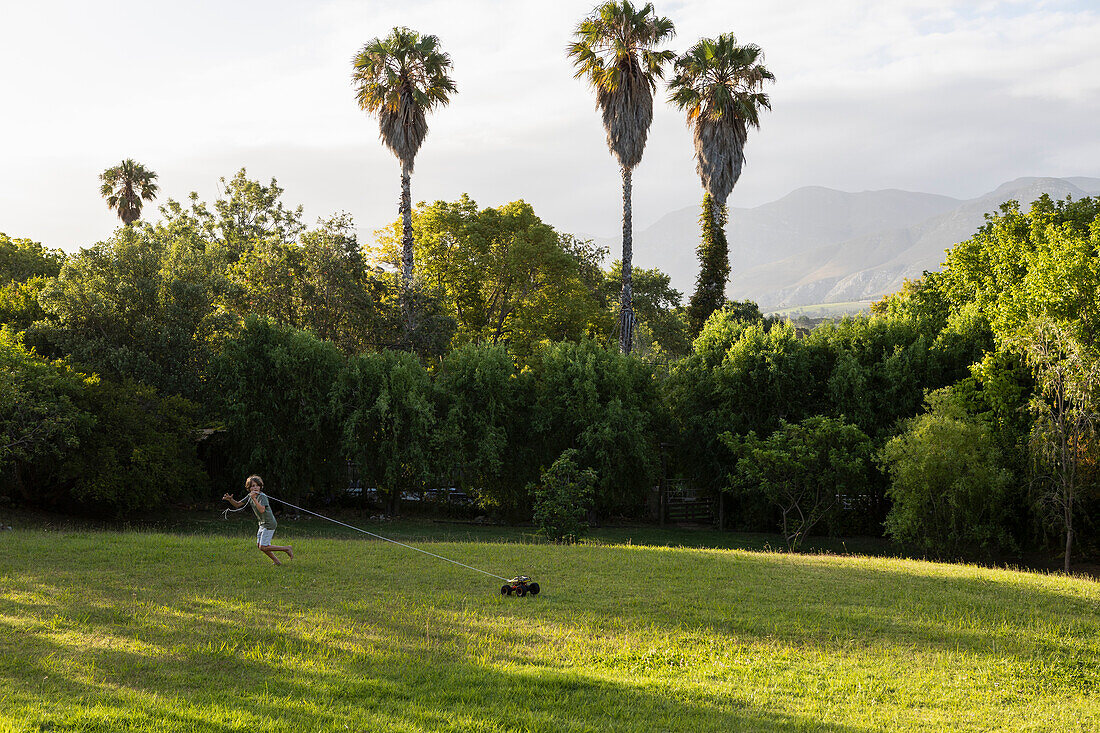 Südafrika, Stanford, Junge (8-9) zieht Spielzeugauto auf großem grünem Rasen