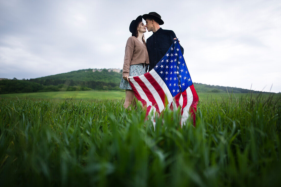 Junges Paar mit amerikanischer Flagge, das sich in einem Weizenfeld küsst