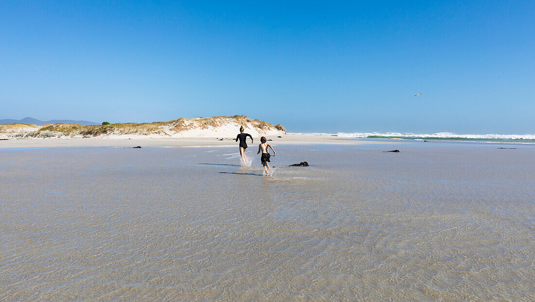 South Africa, Hermanus, Girl (16-17) and boy (8-9) running on Grotto Beach