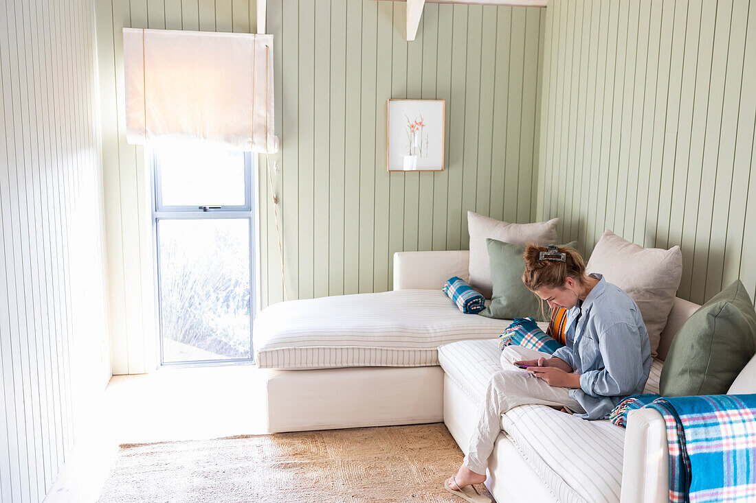 Teenage girl (16-17) sitting on sofa and using phone