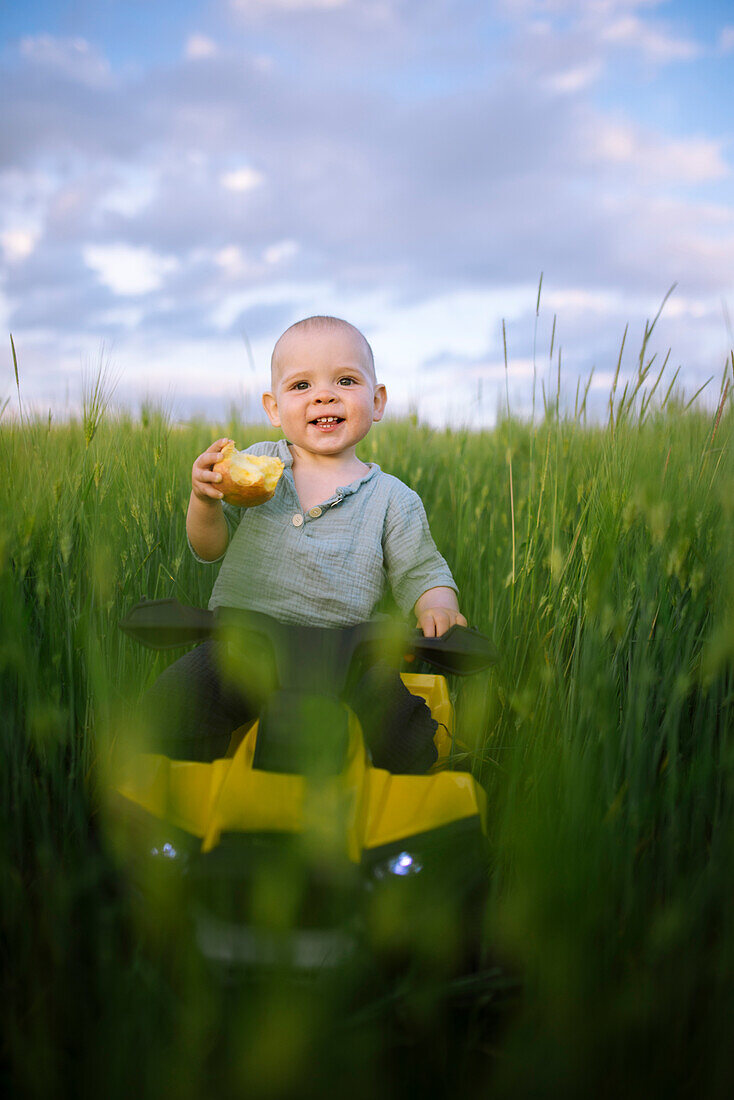 Baby boy (12-17 months) on toy vehicle in agricultural field
