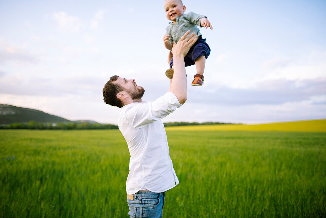 Father playing with baby son (12-17 months) in agricultural field