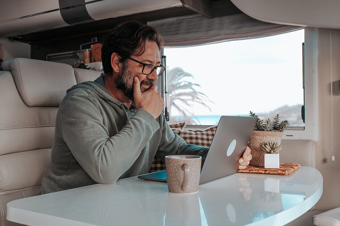 Mann sitzt im Wohnmobil und arbeitet am Laptop