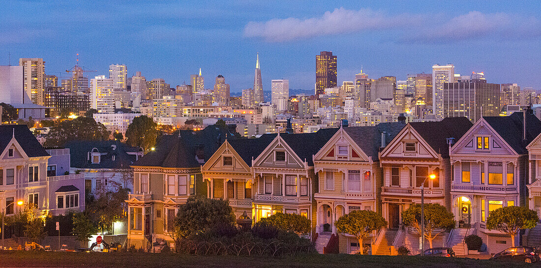 San Francisco, Kalifornien, Painted Ladies, viktorianische Häuser und die Stadt im Hintergrund am Alamo Square an der Hayes Street und Steiner Street bei Sonnenuntergang