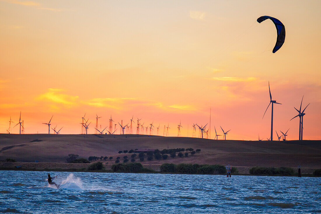 Usa, California, Rio Vista, Sacramento River Delta. Kiteboarder at sunset with wind farm turbines in background.