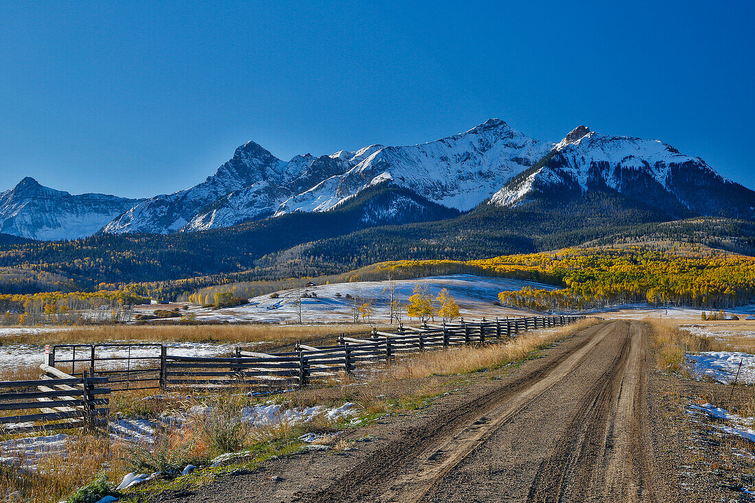 Fence Line and dirt road Dallas Mountain road and San Juan Mountain Range, Colorado, Autumn colors and aspens glowing gold.