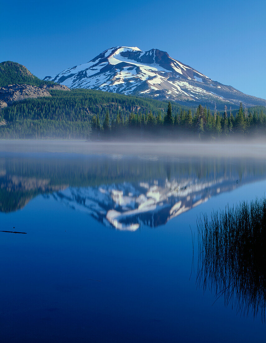 USA, Oregon, Deschutes National Forest, South Sister spiegelt sich im nebligen Wasser des Sparks Lake am frühen Morgen.