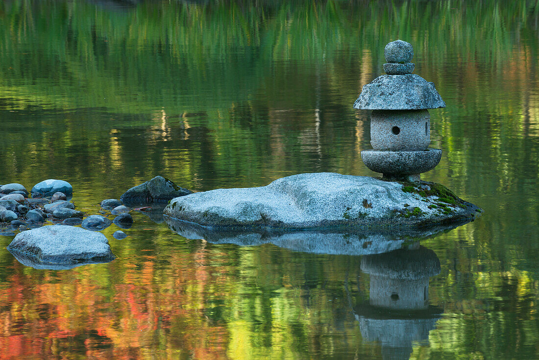 Betonlaterne auf einem Felsen in einem Teich, umgeben von Spiegelungen der Herbstfarben im Wasser, Japanischer Garten, Washington Park Arboretum, Seattle, Washington State