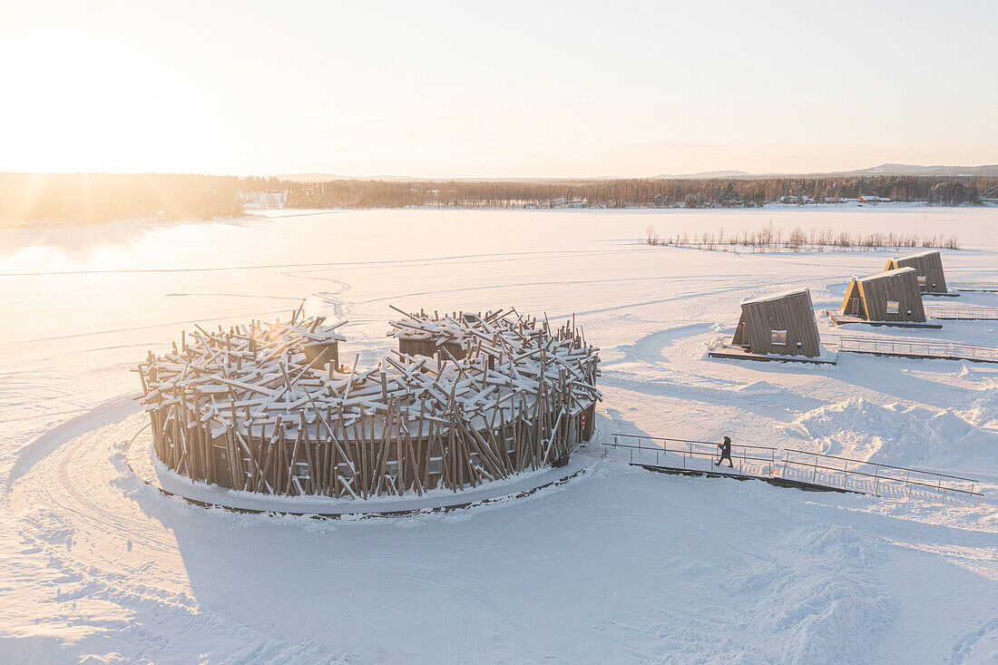 Person auf dem Weg zum schwimmenden Arctic Bath Spa Hotel auf dem gefrorenen Gehweg im Schnee bei Sonnenuntergang, Harads, Lappland, Schweden, Skandinavien, Europa