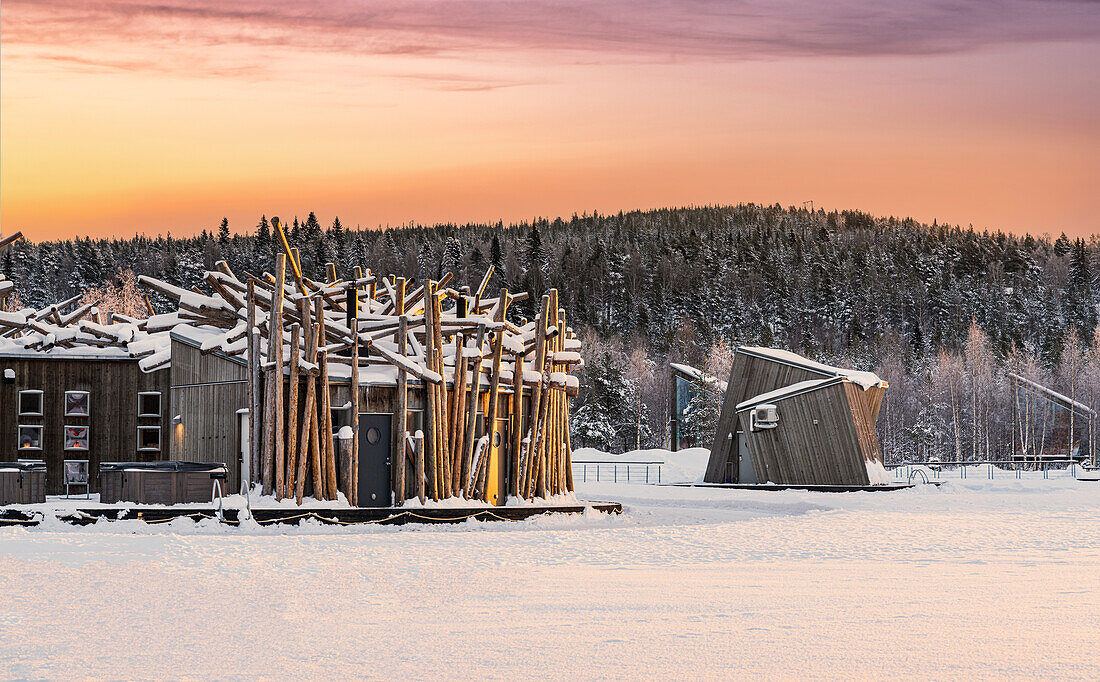 Romantischer Himmel in der Morgendämmerung über dem Arctic Bath Hotel und den schwimmenden Hütten auf dem gefrorenen, mit Schnee bedeckten Fluss, Harads, Lappland, Schweden, Skandinavien, Europa