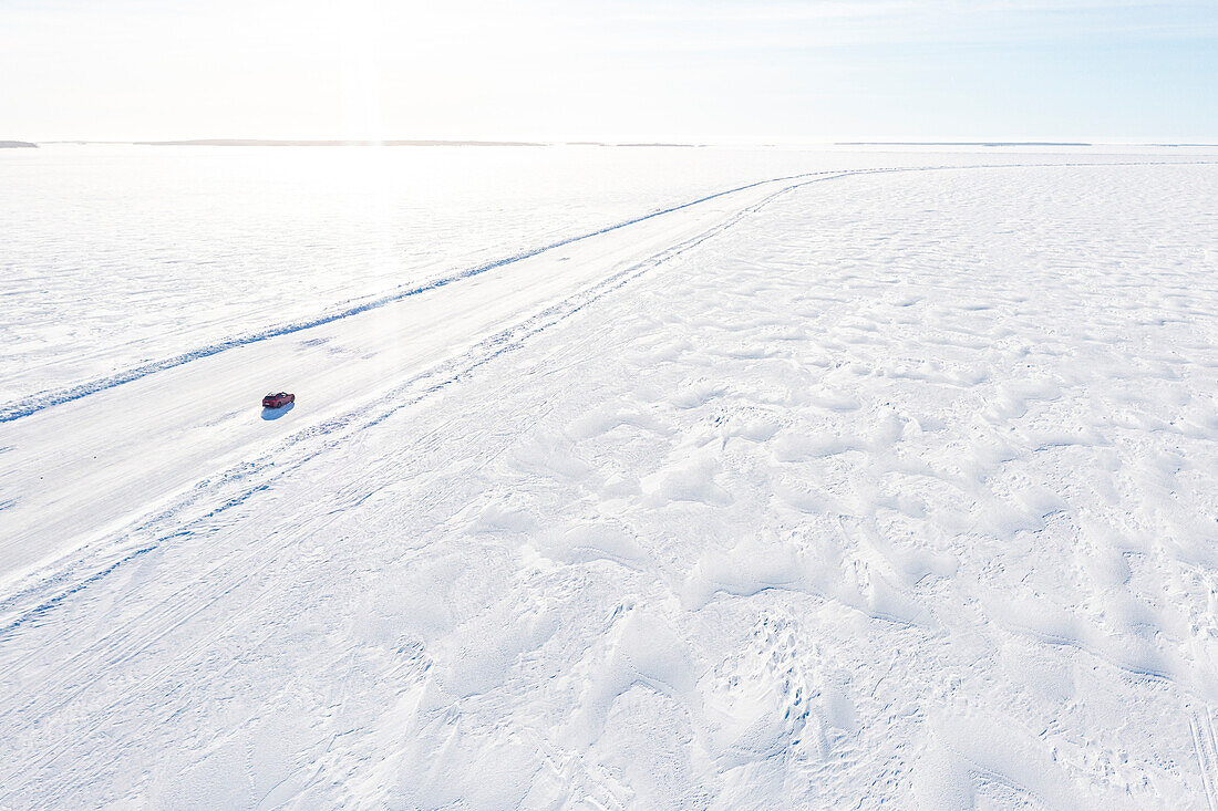 Luftaufnahme eines Autos, das auf einer glatten Eisstraße auf dem zugefrorenen arktischen Meer fährt, Lulea, Norrbotten County, Lappland, Schweden, Skandinavien, Europa