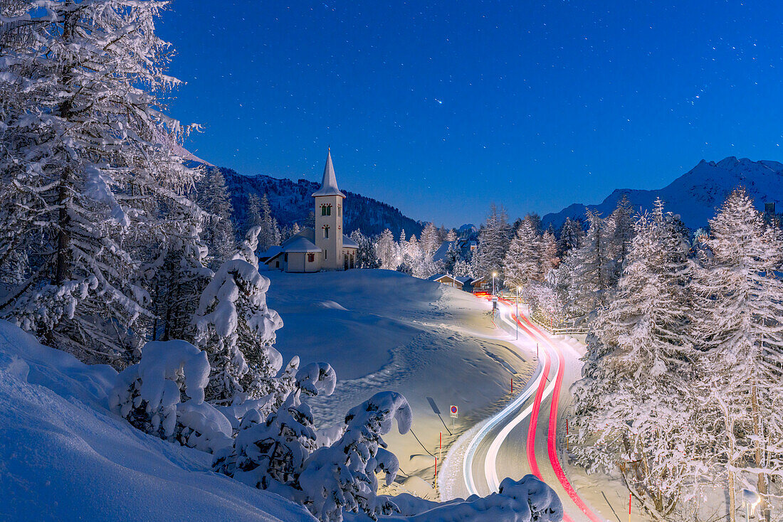 Autospuren Lichter auf verschneiter Bergstraße, die zur Chiesa Bianca führt, unter den Sternen, Maloja, Engadin, Kanton Graubünden, Schweiz, Europa
