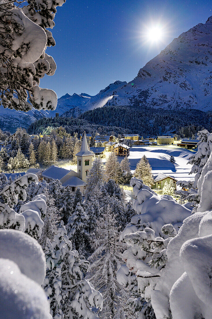 Vollmond über der schneebedeckten Chiesa Bianca, umgeben von Wäldern, Maloja, Bergell, Engadin, Kanton Graubünden, Schweiz, Europa