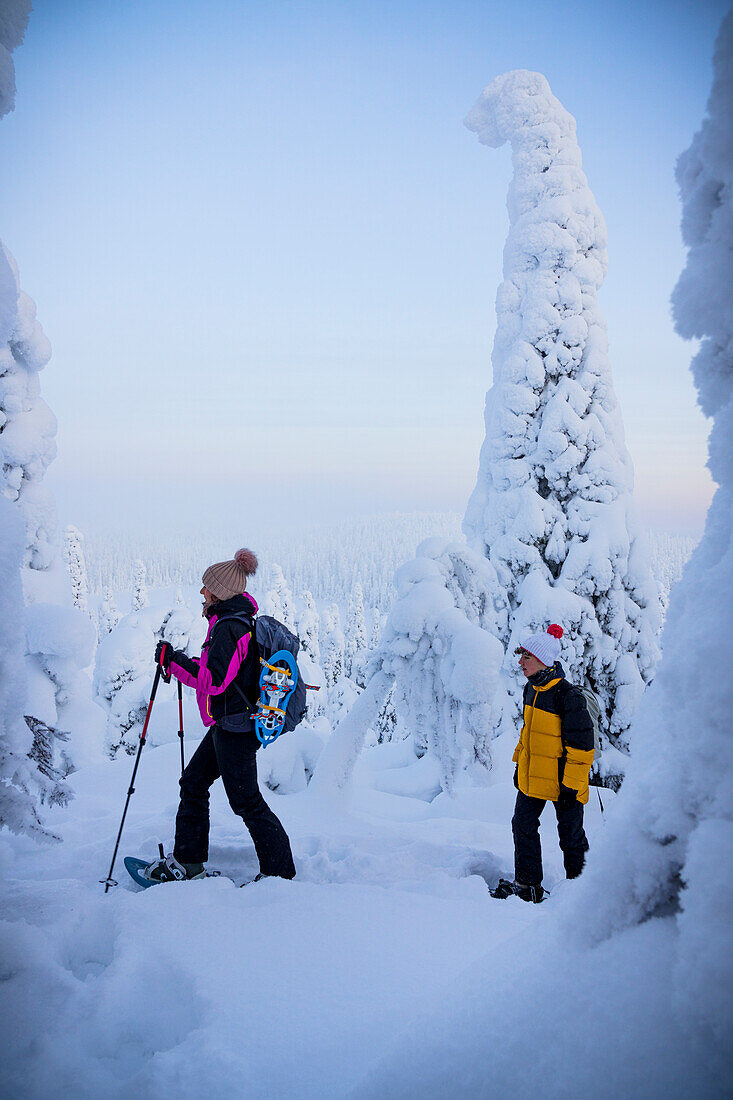 Fröhliche Mutter mit Sohn beim Schneeschuhwandern im gefrorenen Wald, Oulanka-Nationalpark, Ruka Kuusamo, Lappland, Finnland, Europa