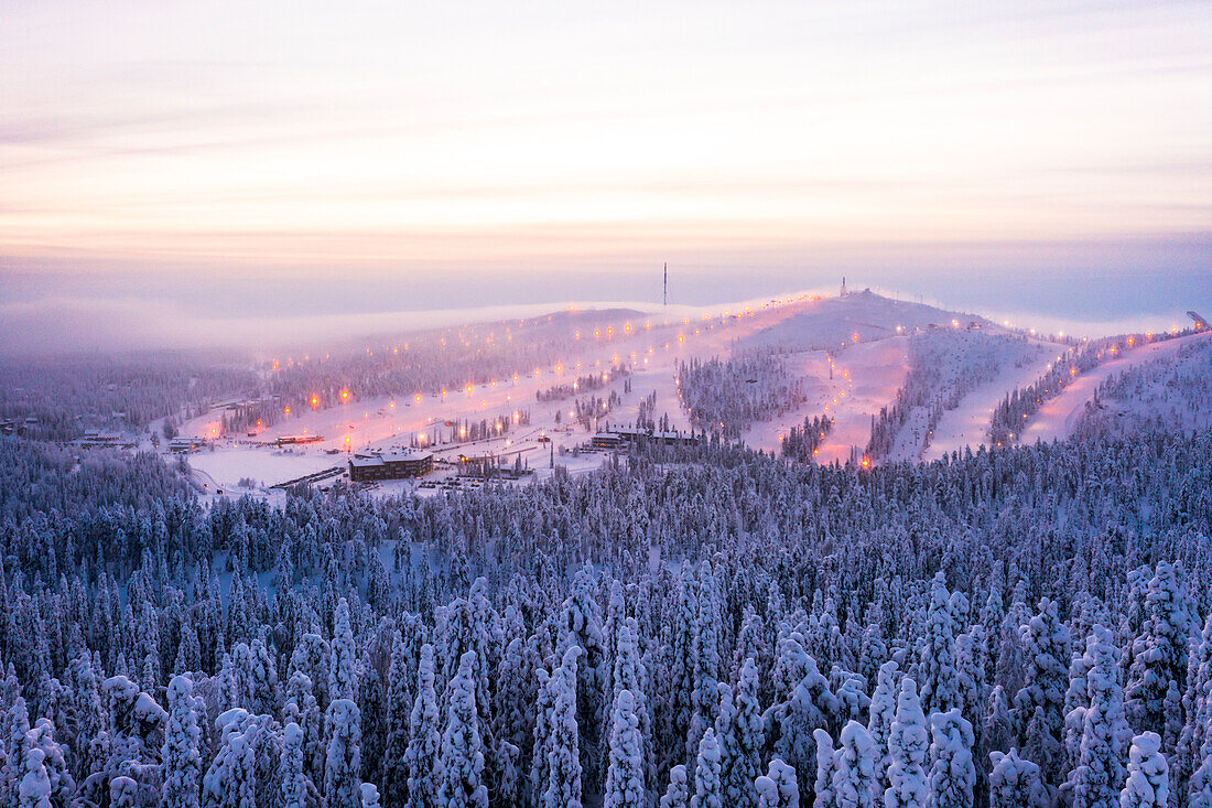 Nebel bei Sonnenuntergang über dem Skigebiet Ruka und verschneiten Wäldern im Winter, Luftaufnahme, Kuusamo, Nordösterbotten, Lappland, Finnland, Europa