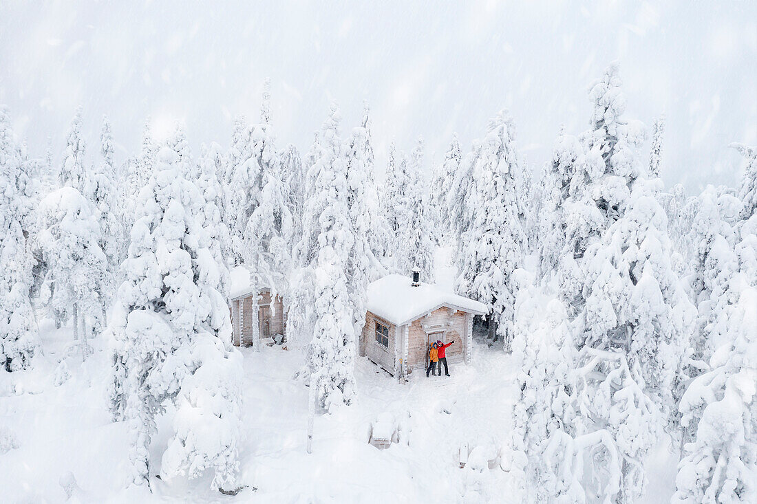 Luftaufnahme eines glücklichen Paares, das den Winterurlaub in einer gefrorenen Hütte im verschneiten Wald genießt, Iso Syote, Nordösterbotten, Lappland, Finnland, Europa