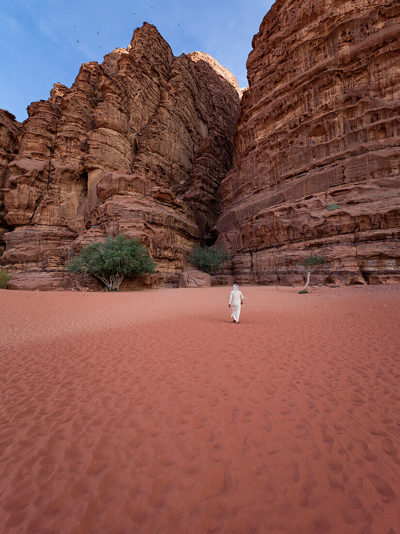 A beduin with traditional white clothes walking towards a canyon in Wadi Rum desert, UNESCO World Heritage Site, Jordan, Middle East