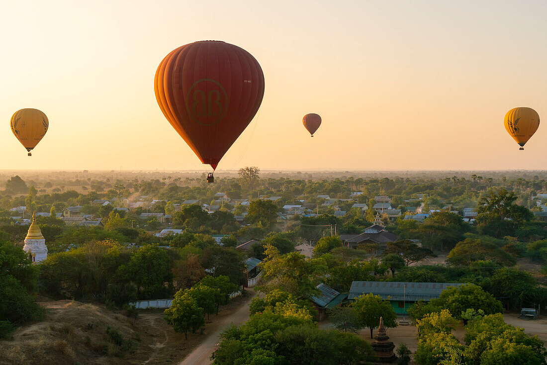 Heißluftballon bei Sonnenaufgang über einem Dorf bei Bagan (Pagan), Myanmar (Burma), Asien