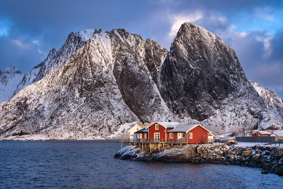 Rote norwegische Rorbuerhütten und der Berg Festhaeltinden im Winter, Reine, Gemeinde Moskenes, Bezirk Nordland, Lofoten, Norwegen, Skandinavien, Europa