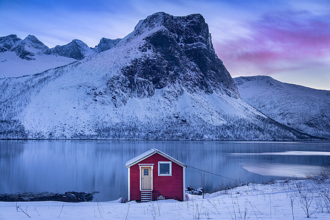 Norwegische Rorbu-Hütte am Ufer des Bergsfjords im Winter, im Hintergrund das Bergsbotn-Gebirge, Bergsbotn, Senja, Troms og Finnmark, Norwegen, Skandinavien, Europa