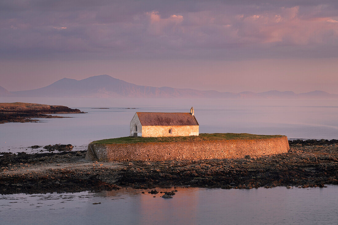 Abendlicht beleuchtet die St. Cwyfan's Church (Kirche im Meer) auf der Insel Cribinau im Hintergrund der Halbinsel Lleyn, nahe Aberffraw, Anglesey, Nordwales, Vereinigtes Königreich, Europa