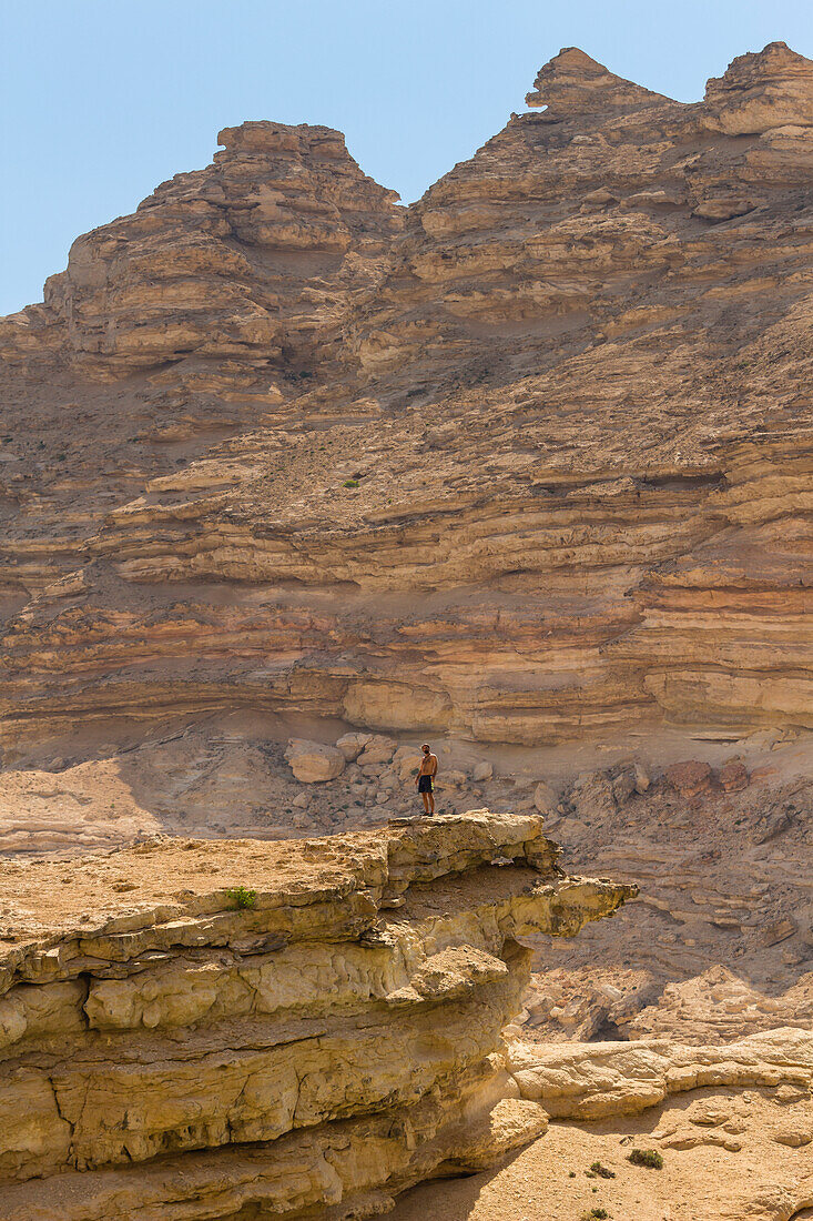 Mann steht auf einer Klippe vor den Bergen, Wadi Sinaq, Dhofar Governorate, Oman, Naher Osten