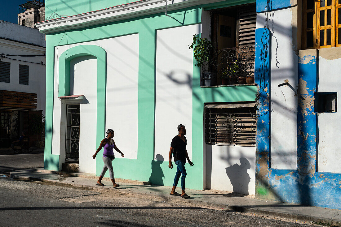 Mann und Frau und ihre Schatten gehen an bunten Gebäuden vorbei, Alt-Havanna, Kuba, Westindien, Karibik, Mittelamerika