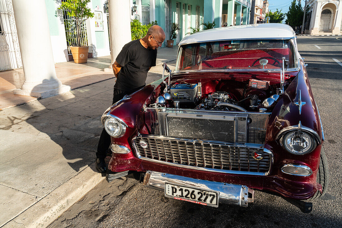 Kubanischer Mann inspiziert und bewundert den offenen Motor eines roten Chevrolet-Klassikers, Cienfuegos, Kuba, Westindien, Karibik, Mittelamerika