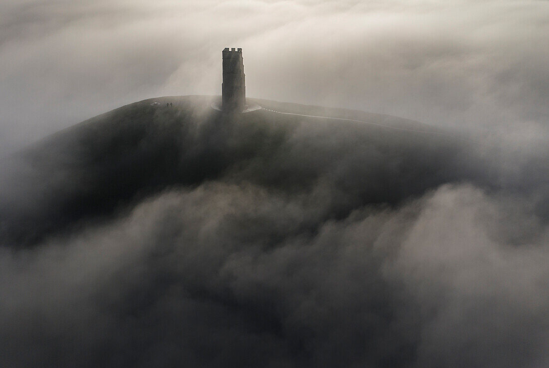 Luftaufnahme des St. Michael's Tower auf dem Glastonbury Tor, umgeben von einem Nebelmeer im Winter, Glastonbury, Somerset, England, Vereinigtes Königreich, Europa