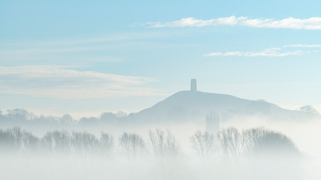 St. Michael's Tower auf dem Glastonbury Tor über dem Turm der St. John the Baptist's Church an einem nebligen Morgen im Winter, Glastonbury, Somerset, England, Vereinigtes Königreich, Europa