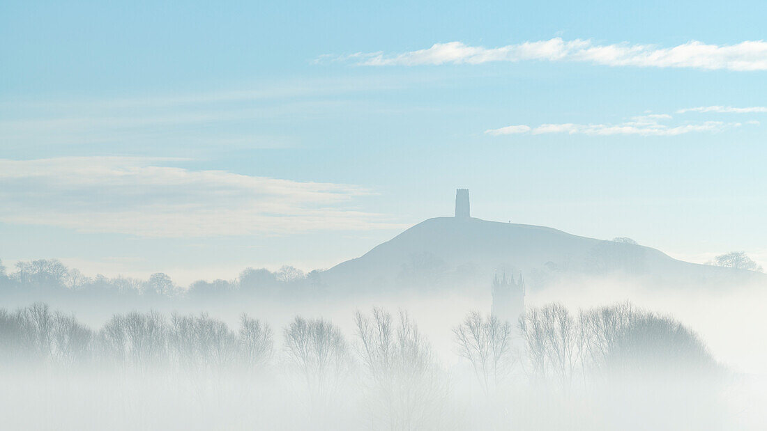 St. Michael's Tower on Glastonbury Tor above the tower of St. John the Baptist's Church on a misty morning in winter, Glastonbury, Somerset, England, United Kingdom, Europe