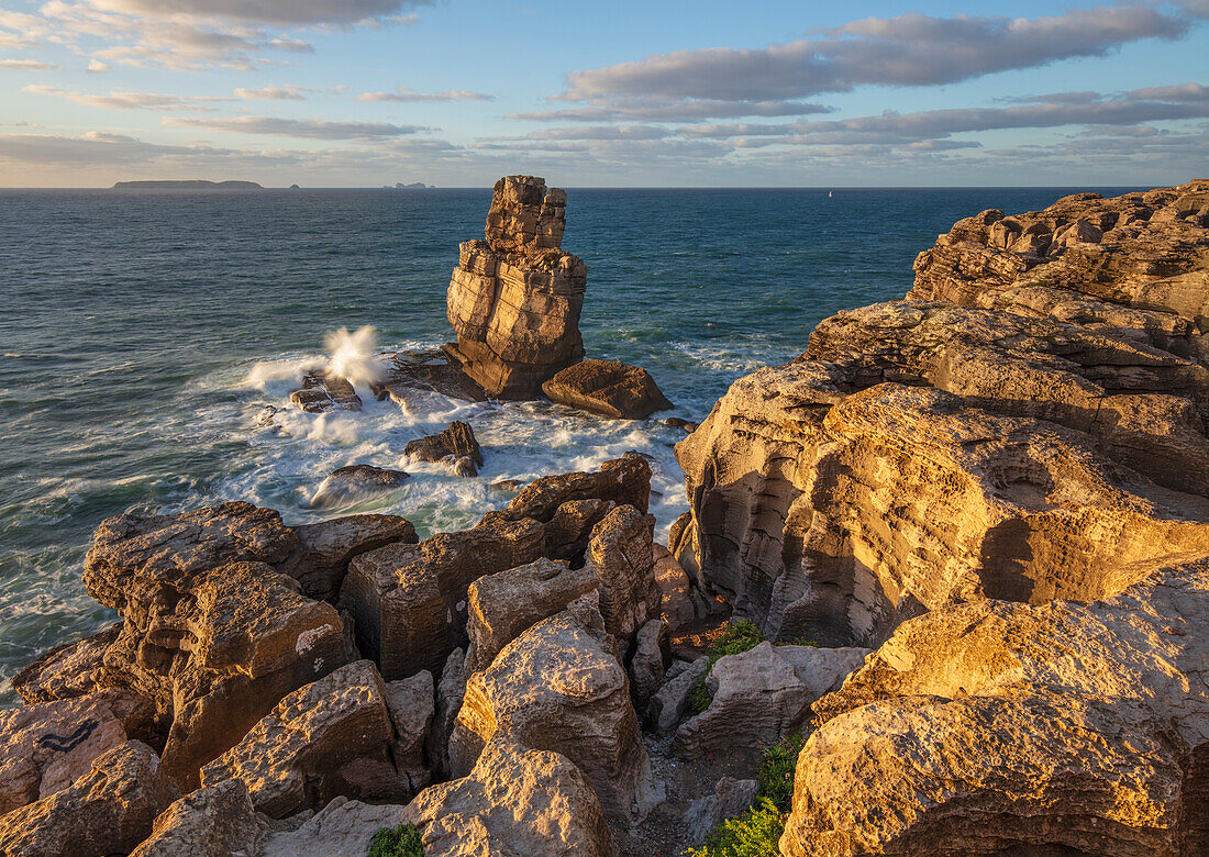 Waves crashing against rock stack at Cabo Carvoeiro in evening sunlight with Ilha da Berlenga in the distance, Peniche, Centro Region, Estremadura, Portugal, Europe