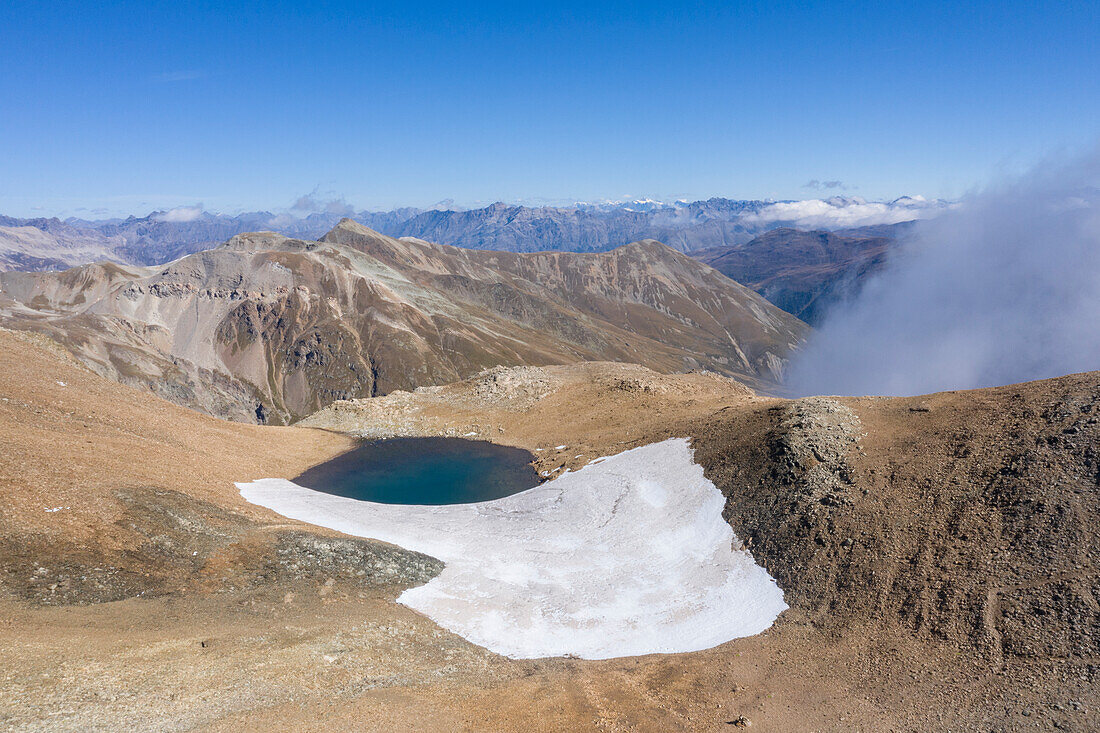 Kleiner See mit Schnee direkt unter dem Gipfel des Monte Breva, Livigno, Provinz Sondrio, Valtellina, Lombardei, Italien, Europa